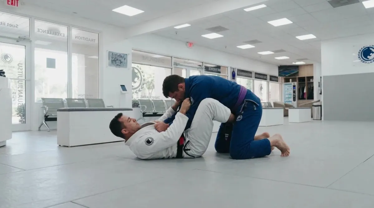 A blue belt on the bottom with legs locked around a partner while pulling his collar to break posture