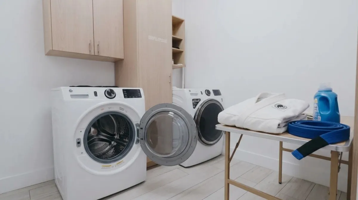 A clean white gi folded neatly on a laundry table beside a front-loading washing machine