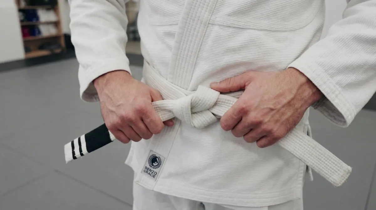 A white belt student listening closely to an instructor explaining a technique on gray mats