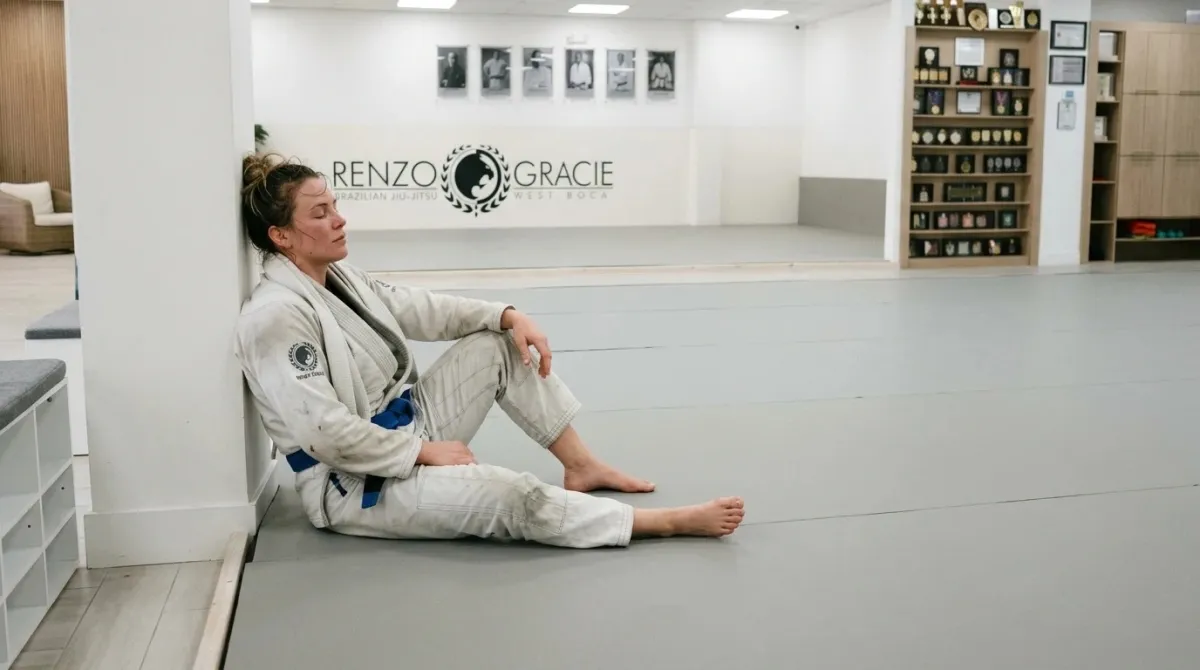 A woman resting against the wall after class with her eyes closed and a towel over her shoulders
