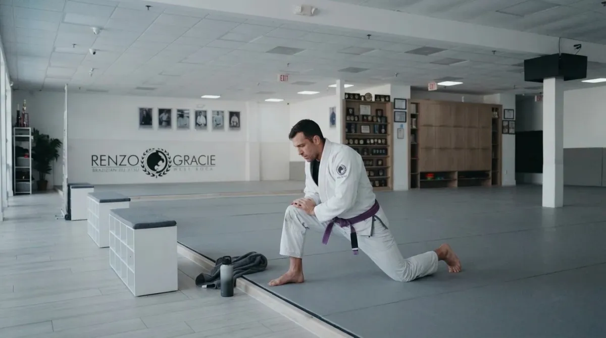An adult man in a lunge stretch alone on the edge of a gray mat in soft morning light
