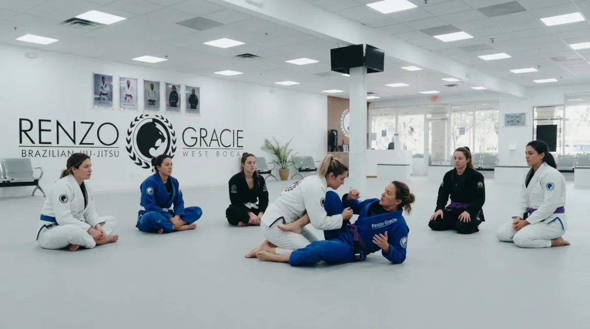 An instructor showing half guard to a group of adult women seated on the mat