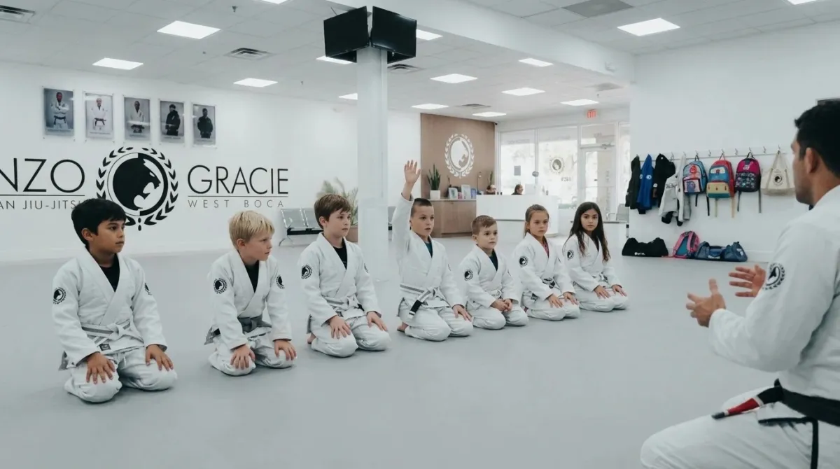 Children sitting in a neat row on the mat watching an instructor demonstrate a movement
