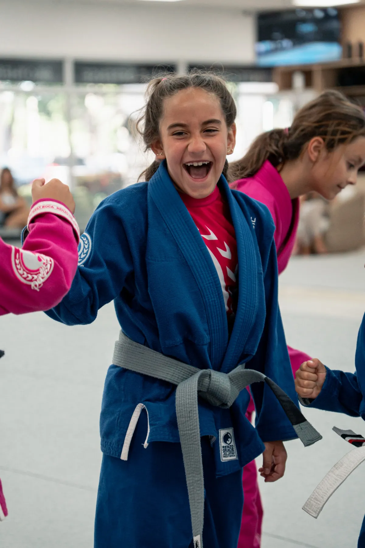 Niña sonriendo con kimono azul y cinturón gris, riendo con sus compañeros