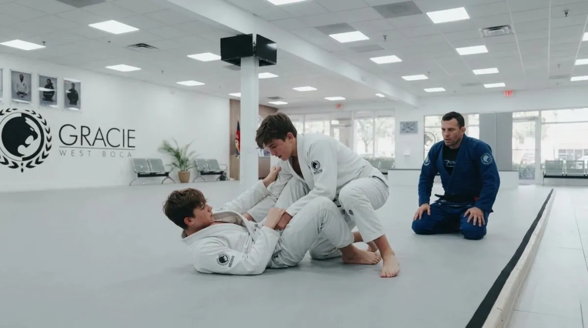 Two teenage boys drilling a technique on gray mats with an instructor watching