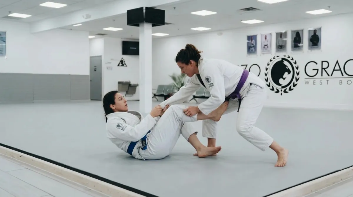 Two women on the mat: one in guard using her feet on the hips to block while the other tries to pass